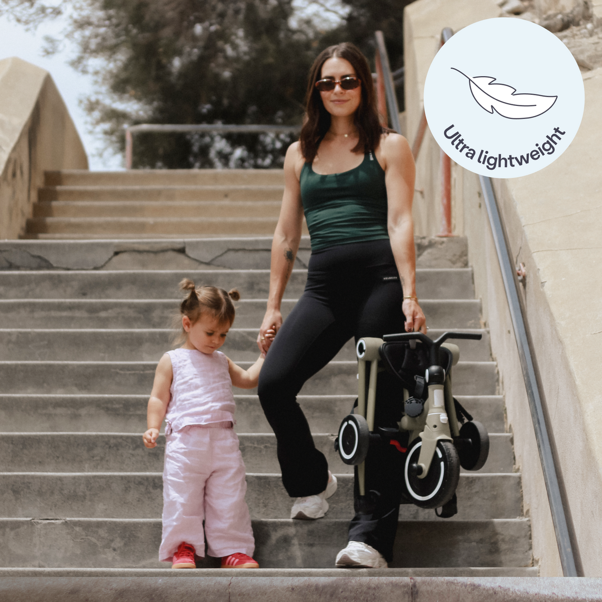 A parent carrying a folded Wonder down steps beside a walking toddler