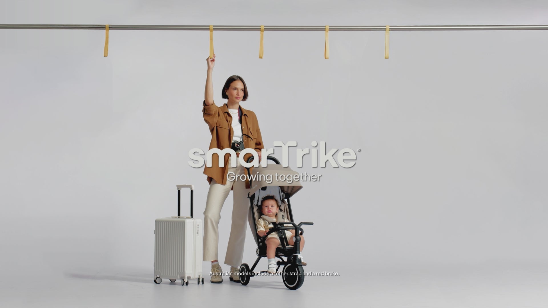 A parent holding a train strap beside a suitcase and a toddler in a Wonder stroller-trike