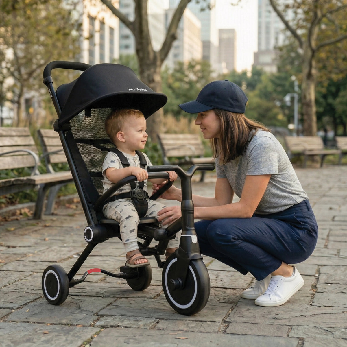 A parent crouching beside a toddler in a smarTrike in a city park