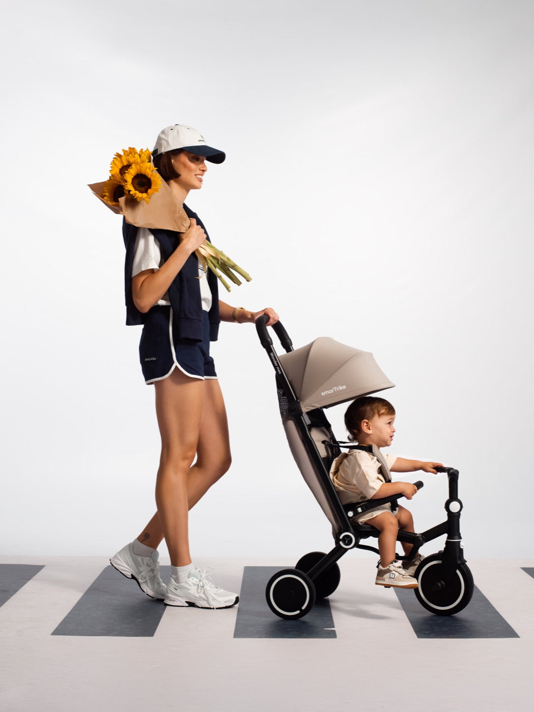 Parent pushing a Wonder max in Stone Beige across a pedestrian crossing, carrying sunflowers
